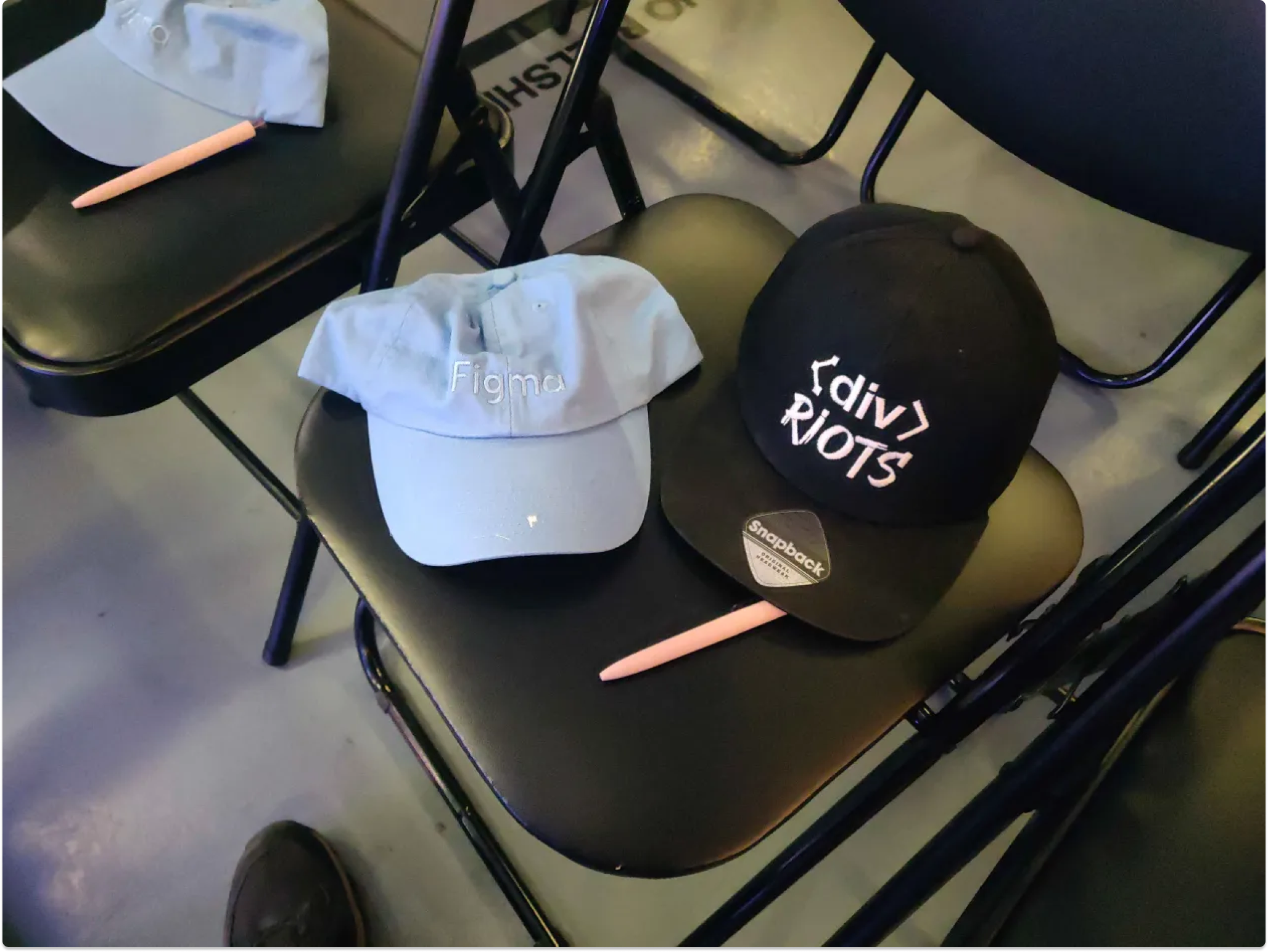 Photo of divRIOTS branded hat next to a Figma branded hat on a chair.